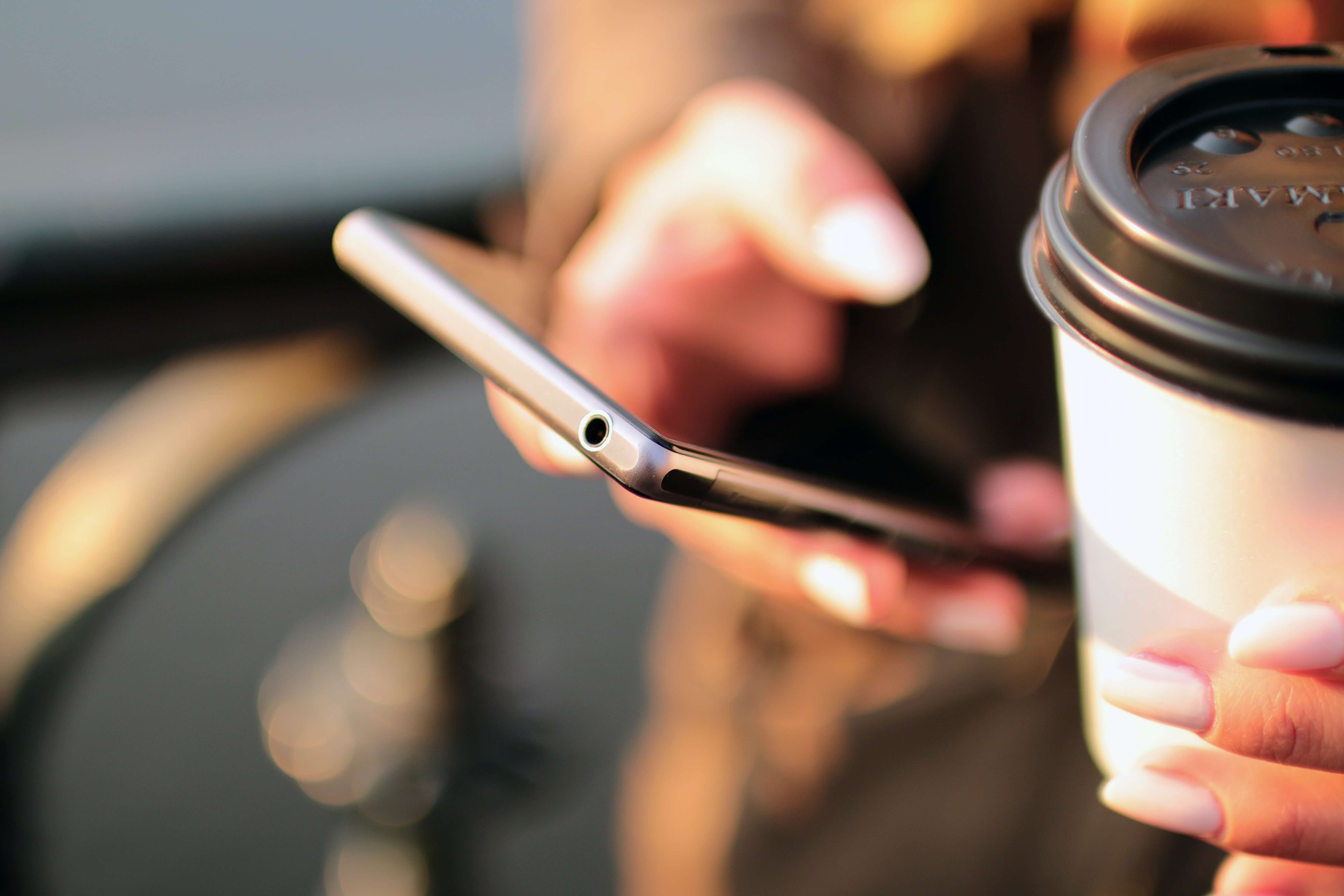 A semi-blurred photograph of hands holding a smartphone to contact Mixam and a coffee cup.