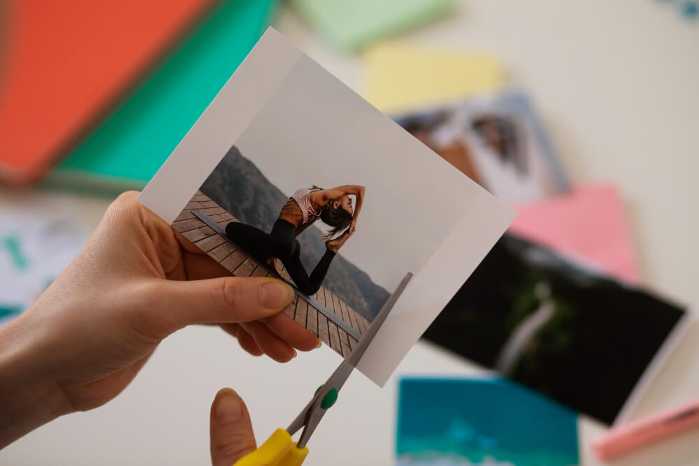 A woman holds a photograph for a zine of a woman doing yoga and cuts along the right side.