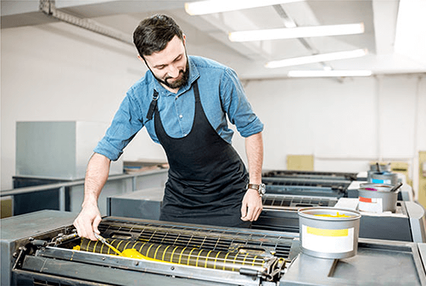 A man adding yellow ink to an offset printer.